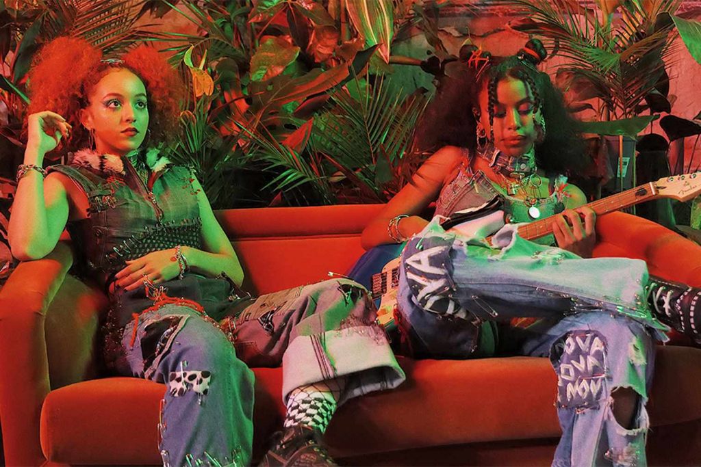 nova twins sitting on couch playing fender guitar